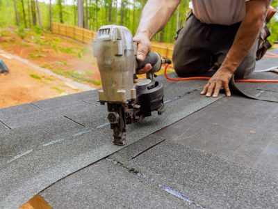 Using an air pneumatic nail gun, roofer install new asphalt bitumen shingles